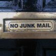Siyah bir kapıdaki metal posta kutusunun üzerinde, spam mail engellemeyi simgeleyen "NO JUNK MAIL" (İstenmeyen Posta Yok) uyarısı bulunuyor.