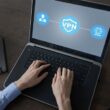 Dizüstü bilgisayar ekranında VPN'in nasıl çalıştığını gösteren bir şema. Kullanıcı simgesi, VPN kalkanı aracılığıyla internete (www) güvenli ve şifreli bir şekilde bağlanıyor.